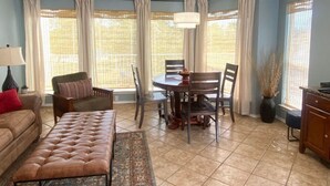 A living room with a sofa, a coffee table, a dining table with chairs, a ceiling fan, and large windows with curtains. - Waterwheel Retreat | Pet Friendly | 3rd Floor (New Braunfels)