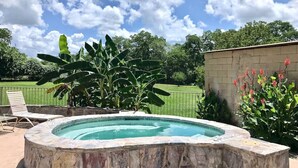 A swimming pool with a stone edge, surrounded by a stone wall, with a grassy lawn and trees in the background. - Waterwheel Retreat | Pet Friendly | 3rd Floor (New Braunfels)