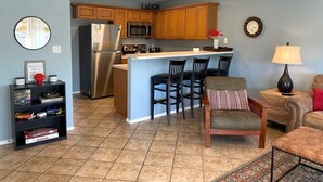 A modern kitchen with wooden cabinets, a stainless steel refrigerator, and a central island with bar stools. - Waterwheel Retreat | Pet Friendly | 3rd Floor (New Braunfels)