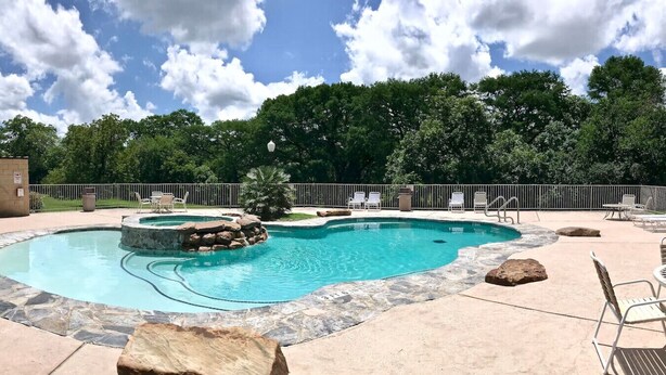 A swimming pool with a stone border, surrounded by lounge chairs and a stone rock feature. - Waterwheel Retreat | Pet Friendly | 3rd Floor (New Braunfels)