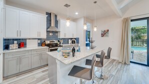 A modern kitchen with white cabinets, a marble island, and bar stools. - New, modern pool villa in Naples Park / 15 min. walk to the beach (Naples)