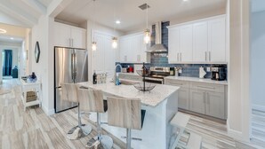 A modern kitchen with white cabinets, a stainless steel refrigerator, and a central island with bar stools. - New, modern pool villa in Naples Park / 15 min. walk to the beach (Naples)