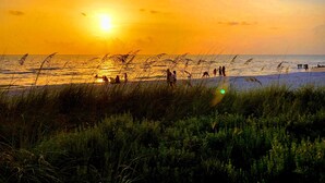 A beach scene with people and grass in the foreground, and a sunset over the water. - New, modern pool villa in Naples Park / 15 min. walk to the beach (Naples)