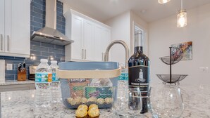 A kitchen with white cabinets, a stainless steel range hood, a blue tiled backsplash, a sink, and a wine bottle. - New, modern pool villa in Naples Park / 15 min. walk to the beach (Naples)