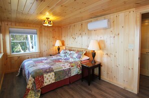 Habitación con paneles de madera, una cama, dos lámparas de noche, un ventanal y un equipo de aire acondicionado.