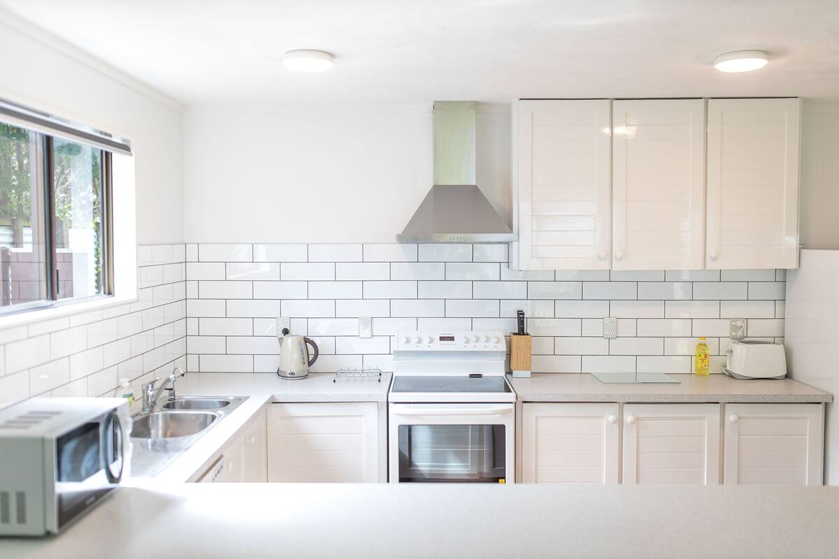 A modern kitchen with white cabinets, a stainless steel range hood, a built-in oven, and a microwave.