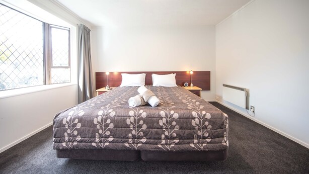 Una habitación de hotel con una cama grande, una ventana con cortinas, una mesita de noche con lámpara y un radiador.