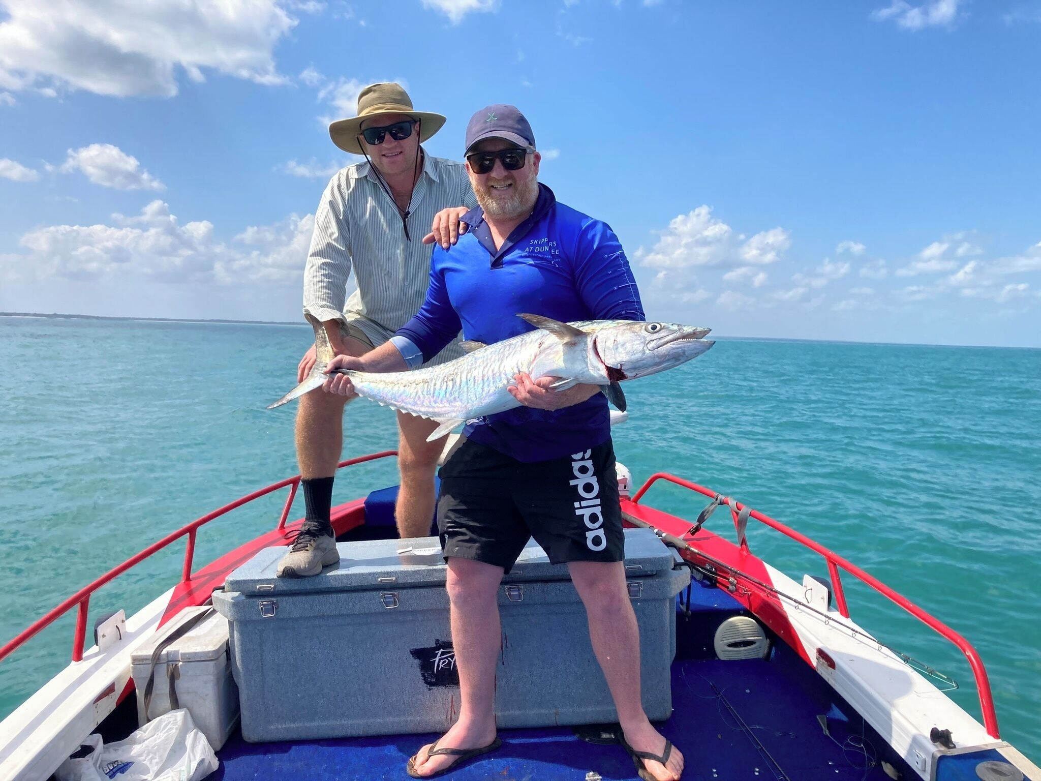 Two people on a boat holding a large fish.