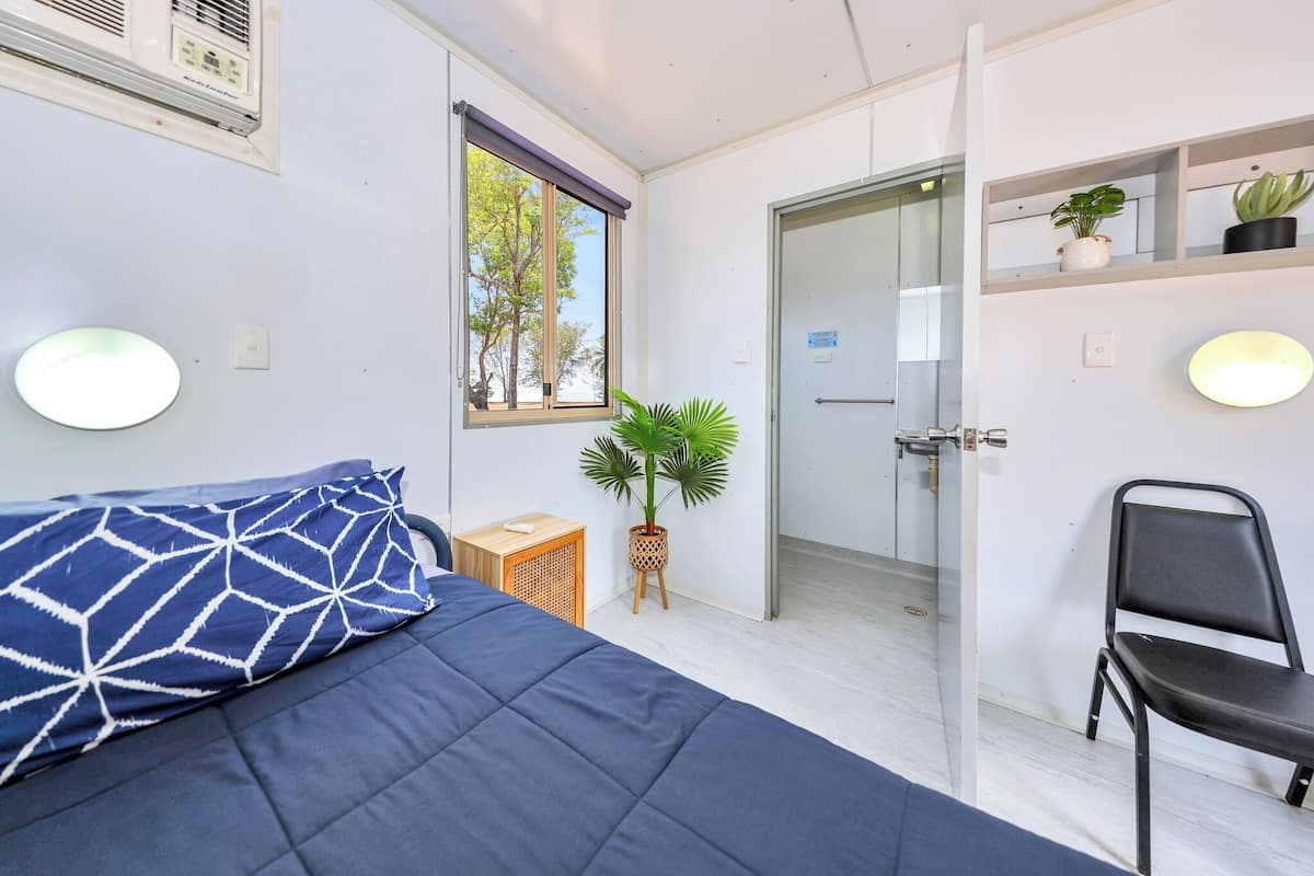 A room with a bed, a chair, a potted plant, a window, and a door.