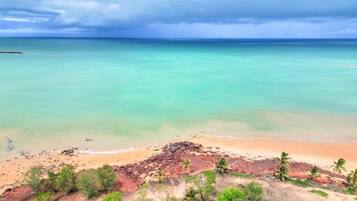 Une plage bordée d’une eau turquoise et limpide, un promontoire rocheux et une végétation clairsemée.