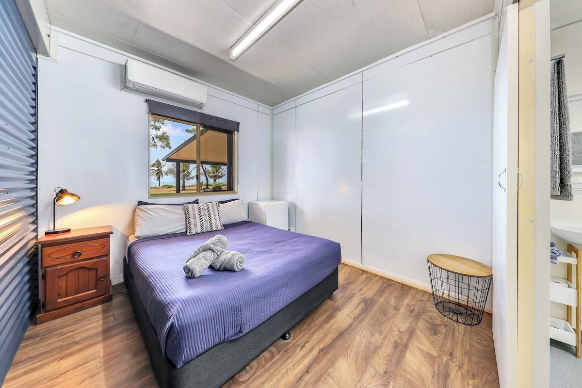 A bedroom with a bed, bedside table, lamp, window, wardrobe, and a small round table.