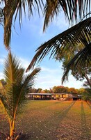 A building with a flat roof and a covered outdoor area, surrounded by grass and palm trees.