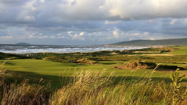 Een golfbaan met uitzicht op de oceaan en een bewolkte lucht.