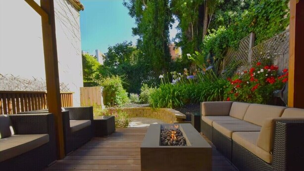 A wooden deck with outdoor furniture, a fire pit, and lush greenery. - Cheerful Suite w/ Garden, Steps from Dolores Park (San Francisco)