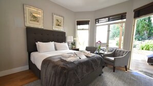 A bedroom with a large bed, a chair, a desk, and a window with a view of greenery. - Cheerful Suite w/ Garden, Steps from Dolores Park (San Francisco)