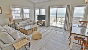 Ein geräumiges Wohnzimmer mit einer großen Couch, einem Couchtisch und einem Fernseher. Ein Balkon bietet Blick auf den Ozean.