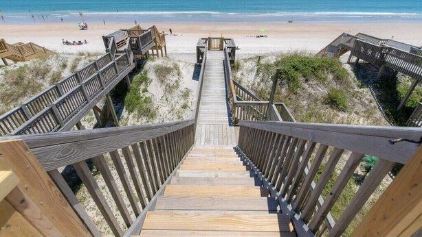 Eine hölzerne Promenade führt zu einem Strand mit freiem Blick auf das Meer.