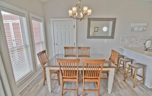 Un coin repas avec une table blanche et des chaises en bois, un lustre, et un espace cuisine comprenant un évier et un plan de travail.