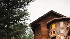 A rustic cabin with a stone facade, wooden deck, and a small waterfall feature. - Juniper Lodge & Treehouses (Evergreen)