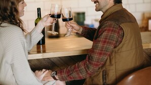 Two people toasting with wine glasses at a bar with a bottle of wine on the counter. - Juniper Lodge & Treehouses (Evergreen)