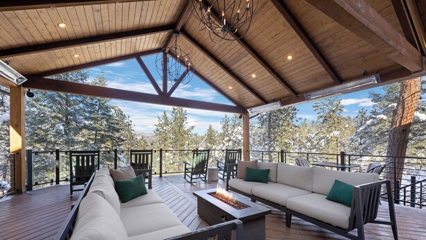 A covered outdoor seating area with a fire feature, wooden deck, and views of snow-covered trees. - Juniper Lodge & Treehouses (Evergreen)