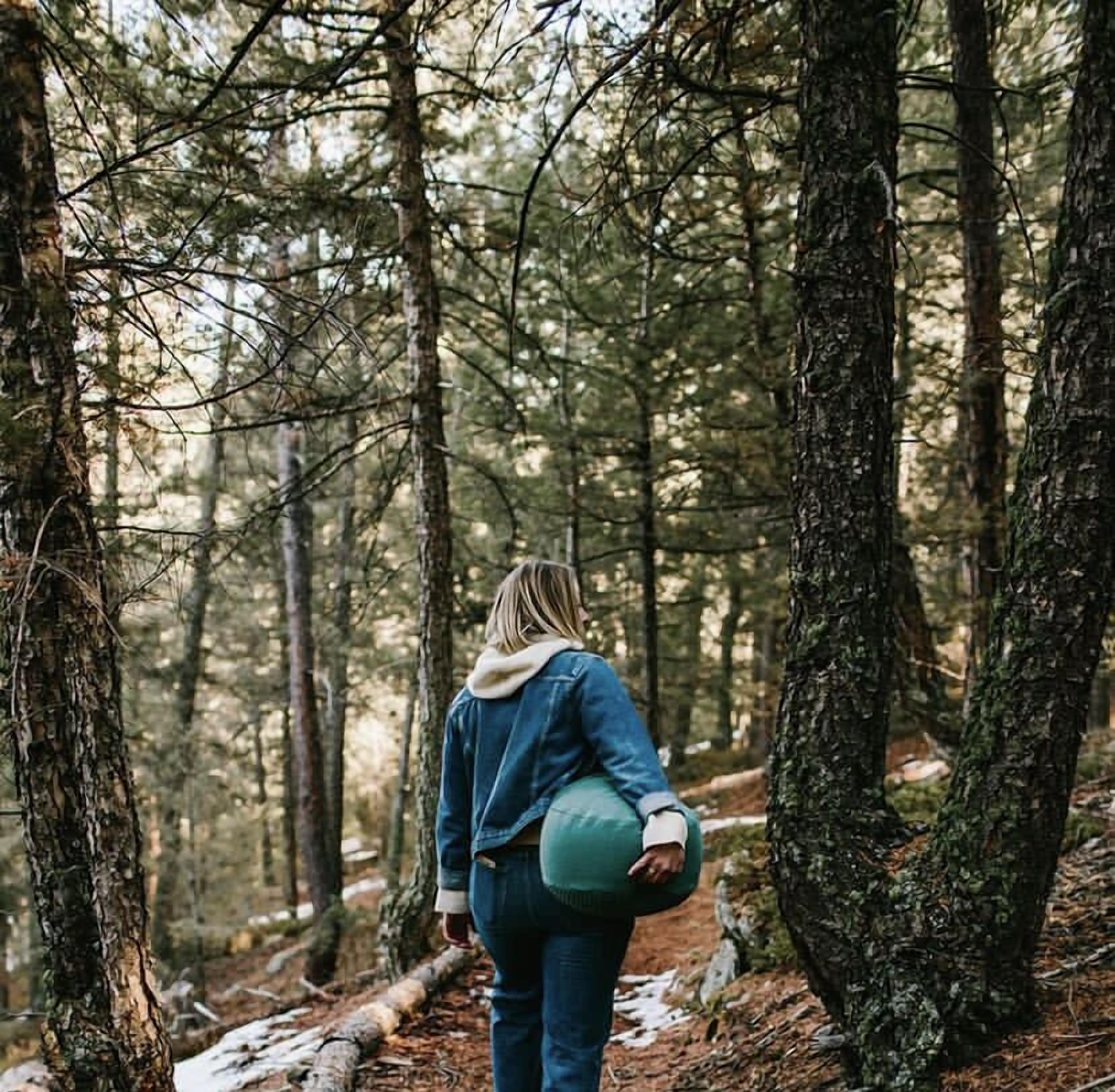 A person walking through a forested area with trees and a fallen log on the ground.