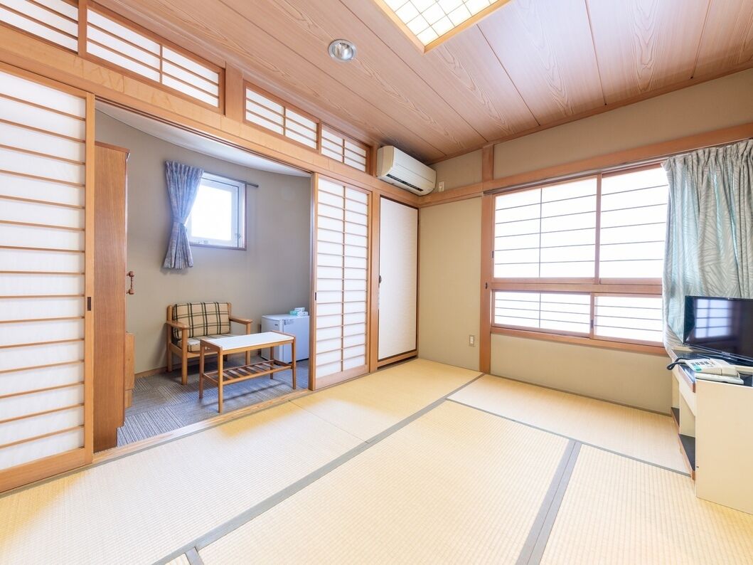 A traditional Japanese room with tatami flooring, a futon bed, a television, and a sliding door.