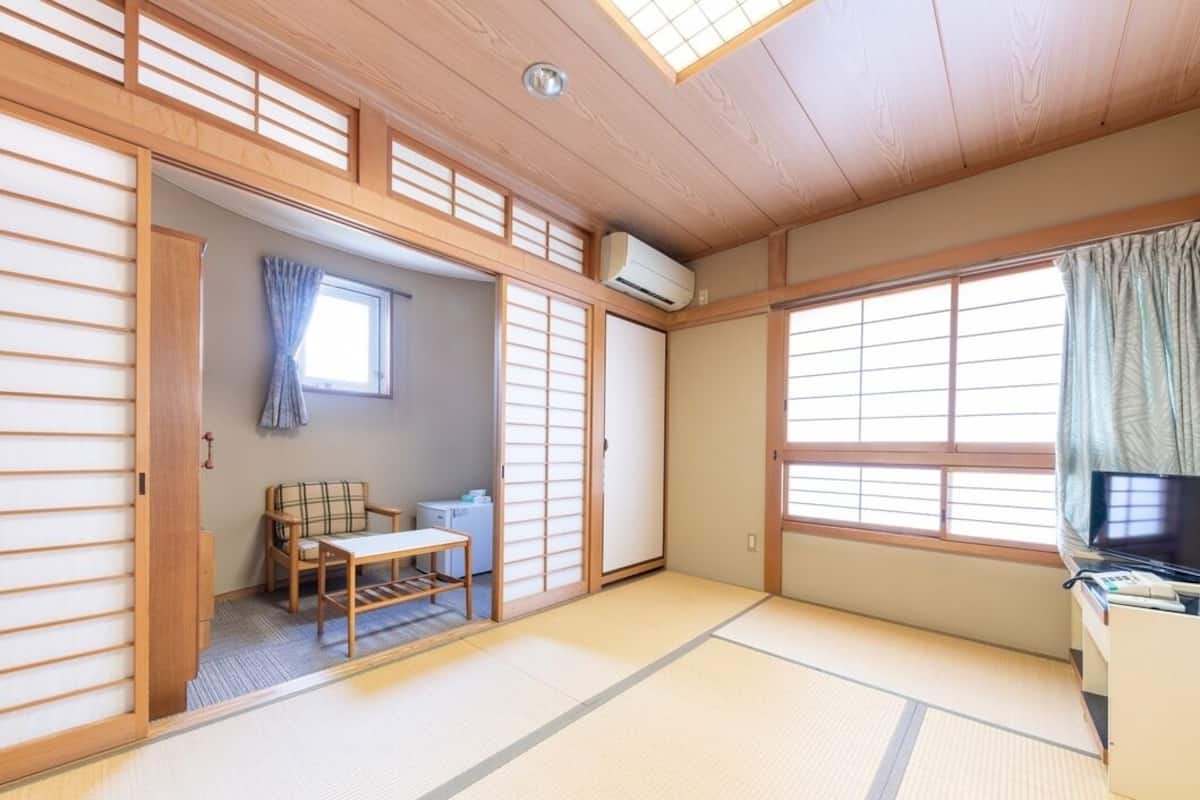 Ett traditionellt japanskt rum med tatamimattor på golvet, en futonmadrass, en tv och en skjutdörr.