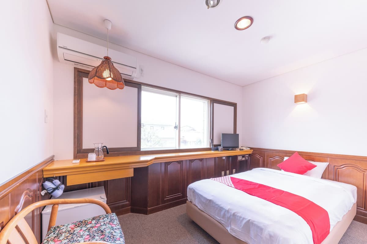 A hotel room with a bed, a desk with a computer, a chair, and a window.
