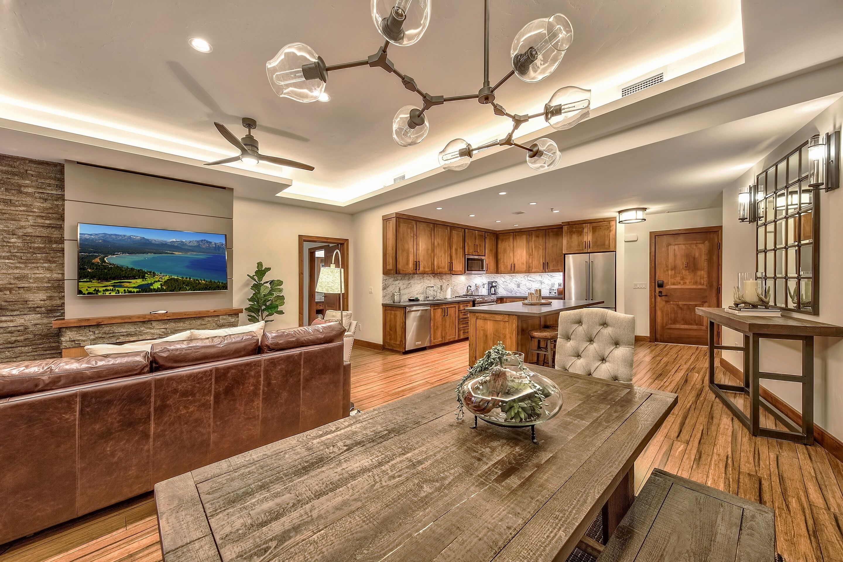 A modern living room with a wooden dining table, leather sofa, and a large flat-screen TV.