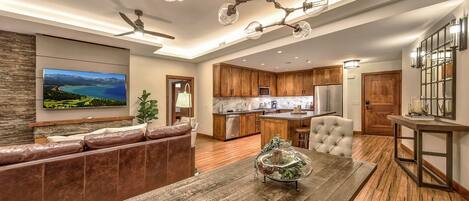 A modern living room with a wooden dining table, leather sofa, and a large flat-screen TV.