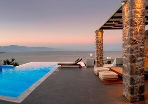 A poolside area with a view of the sea, stone pillars, and lounge chairs. - Beach Front Villa With Large Private Sea Water pool & Amazing Sea View! (Solygeia)