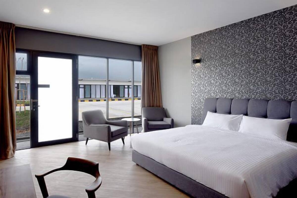 A modern hotel room with a large bed, two armchairs, a small table, and a TV.
