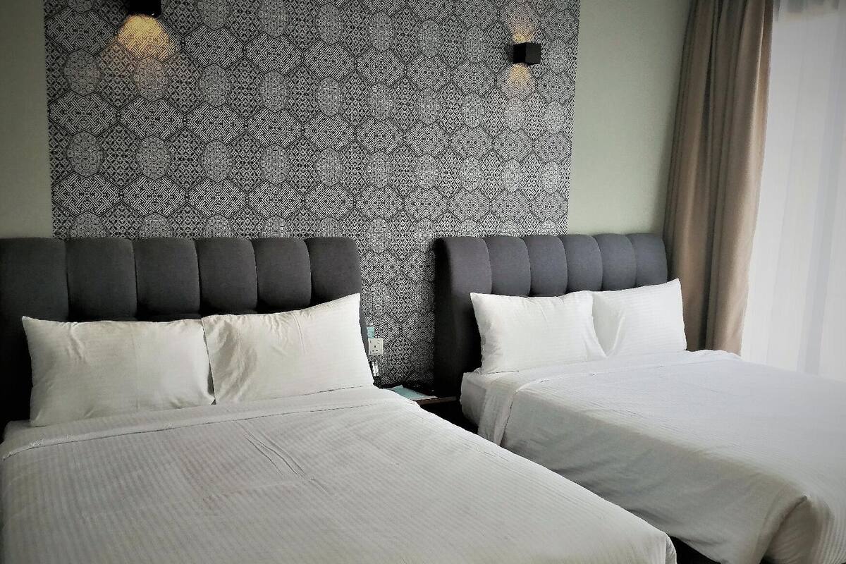 A hotel room with two beds, a patterned wall, and a window with curtains.