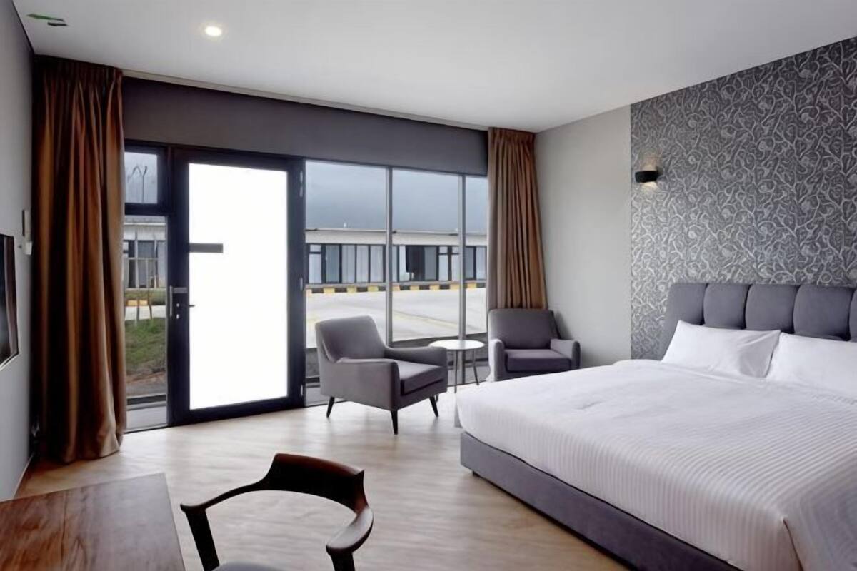 A hotel room with a large bed, two armchairs, a small table, and a view through a large sliding door.