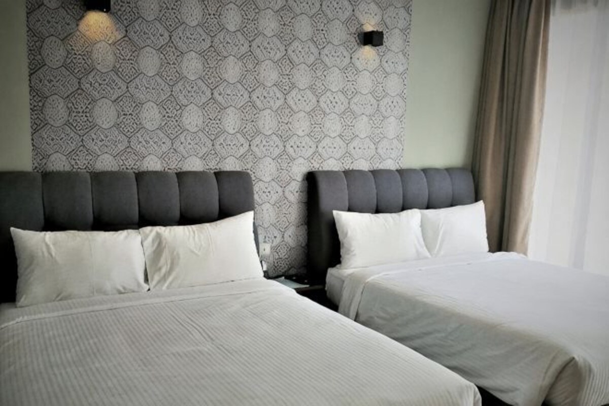 Two beds with headboards, a patterned wall, and a window with curtains.