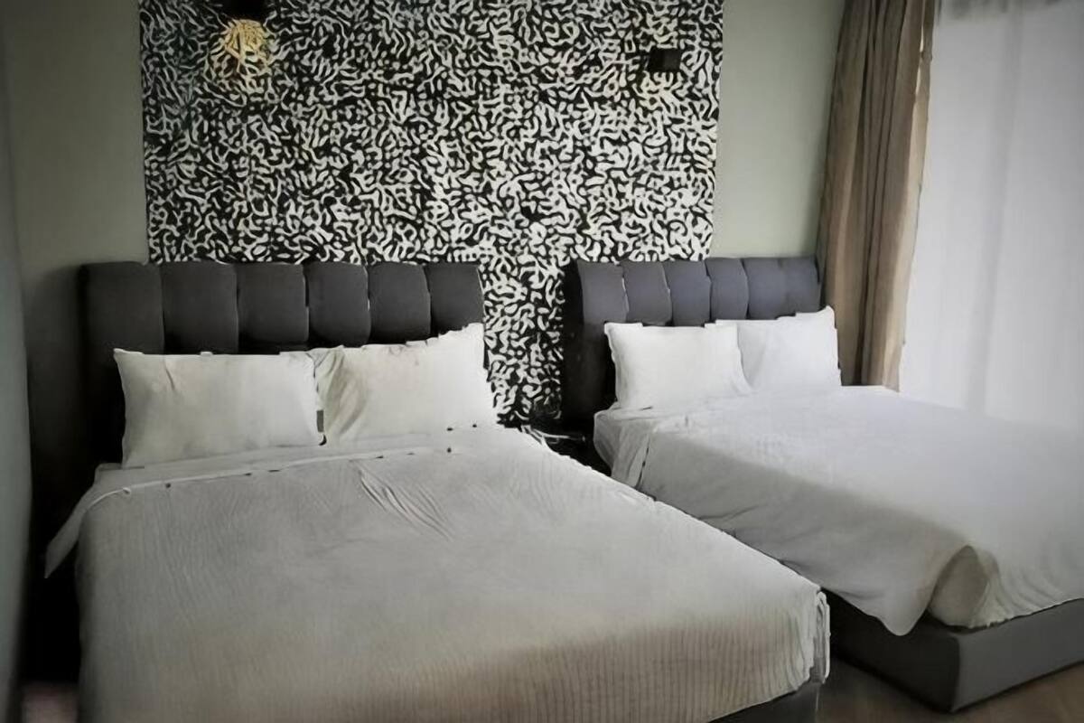 Two beds with headboards, a patterned wall, and a window with curtains.