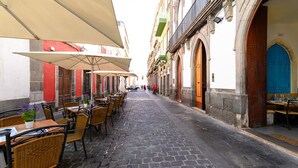 A cobblestone street lined with outdoor seating areas, tables, and chairs, suggesting a dining or café setting.