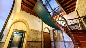 A staircase with a green handrail, an elevator, and a tiled floor.