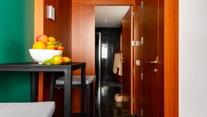 A hotel room with a wooden door, a white bowl of fruit on a table, and a glimpse of a bathroom with a towel hanging.