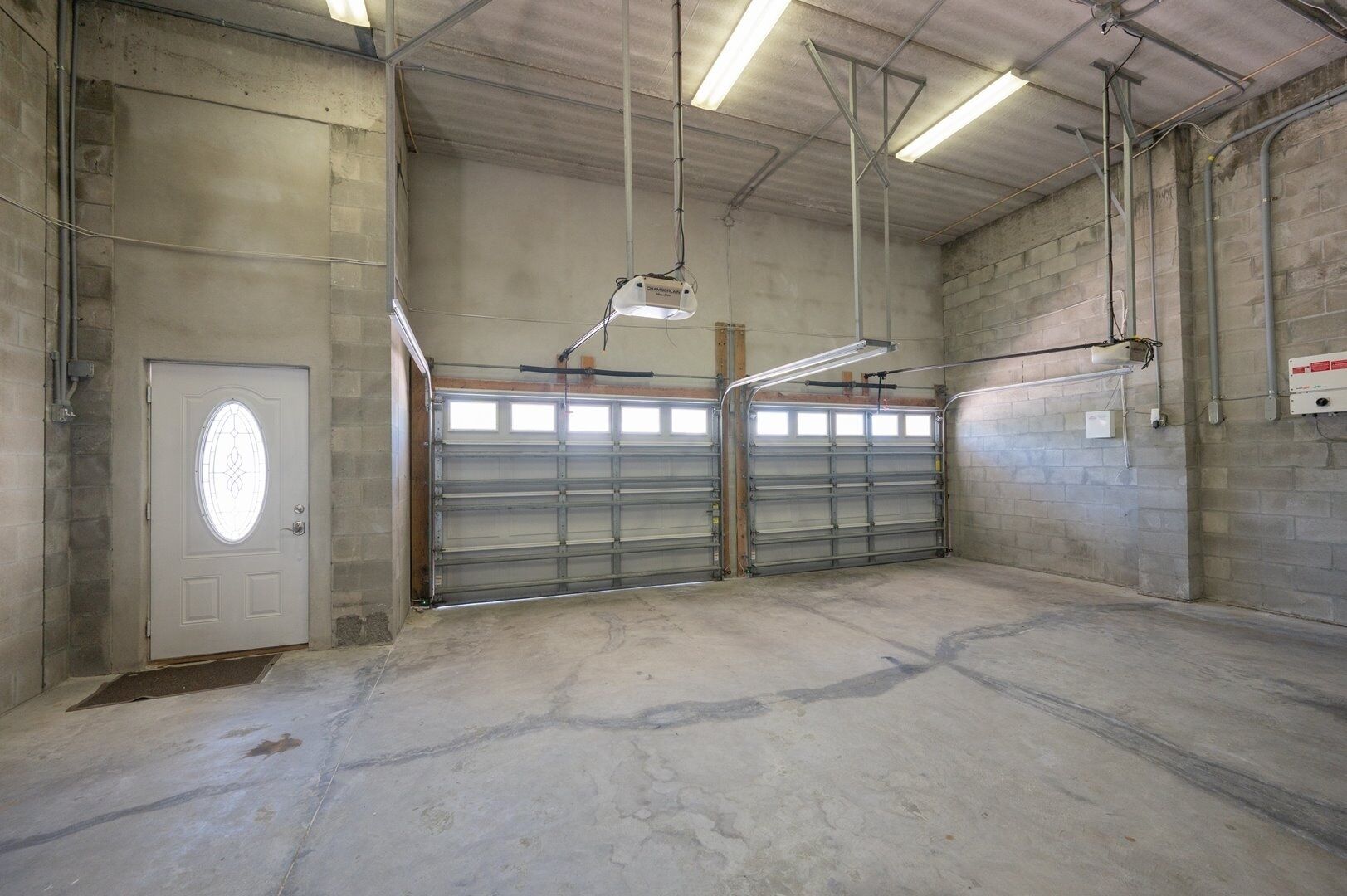 A garage with two metal garage doors, a concrete floor, and overhead fluorescent lighting.