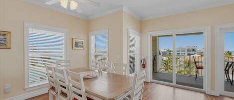 A dining area with a table and chairs, a ceiling fan, and a view through a glass door to an outdoor balcony.