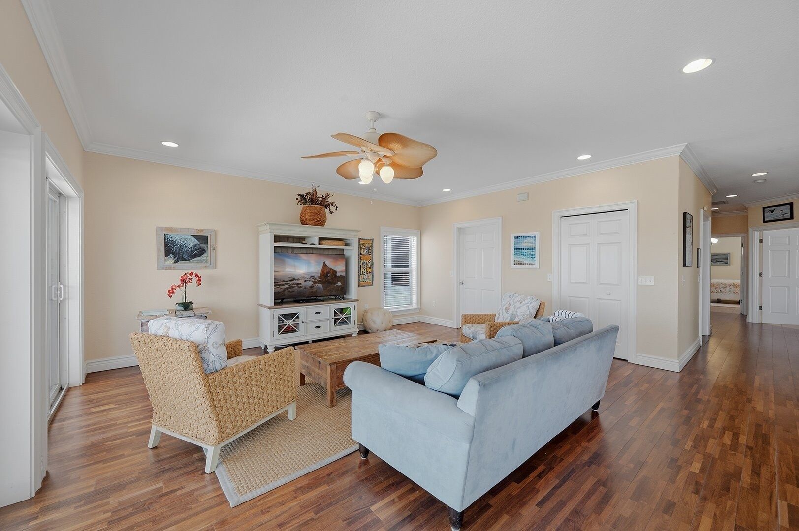 A living room with a sofa, chairs, a TV, and a ceiling fan.