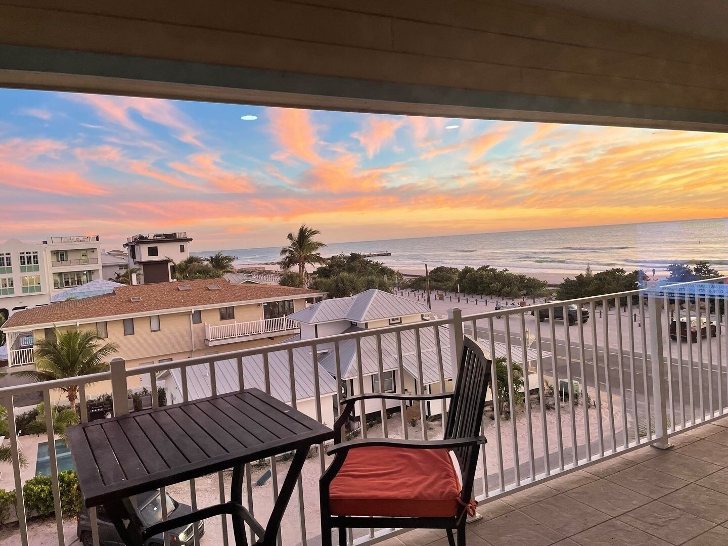A balcony with a view of the ocean and beach, a table, and a chair.