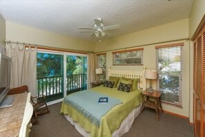 Ein Schlafzimmer mit Bett, Schreibtisch, Stuhl, Fernseher und Balkon.
