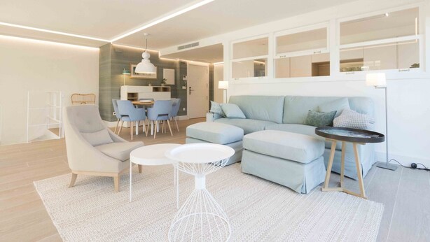 A modern living room with a light blue sofa, a white armchair, and a small white coffee table. There is a dining area in the background with a table and chairs. - Brunet II | The Rentals Collection (San Sebastián)