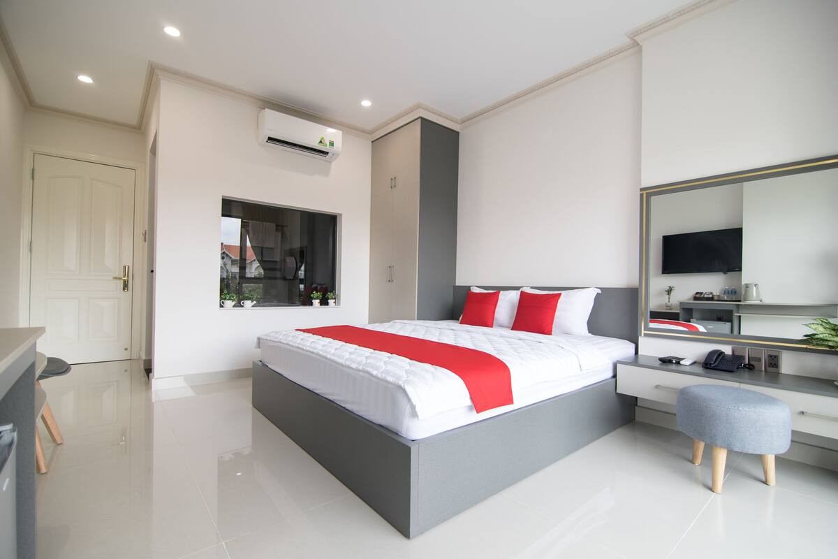 A modern bedroom with a large bed, a desk, a chair, and a TV.