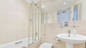 A modern bathroom with a glass shower enclosure, a white bathtub, a sink with a mirror above it, and a toilet. - Little Corner of Bliss in BustlingLondon (London)