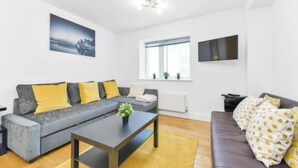 A modern living room with a grey sofa, yellow cushions, a coffee table, and a TV mounted on the wall. - Little Corner of Bliss in BustlingLondon (London)