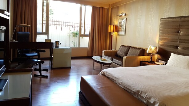 A hotel room with a bed, a sofa, a desk with a chair, a small table, and a lamp. - Gueylin Hotel (Taoyuan City)